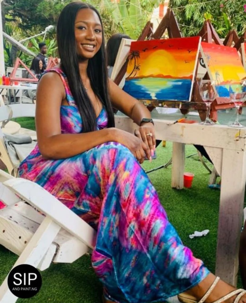 A guest seated in the garden at a Sip and Paint Abuja session with her sunset seascape canvas