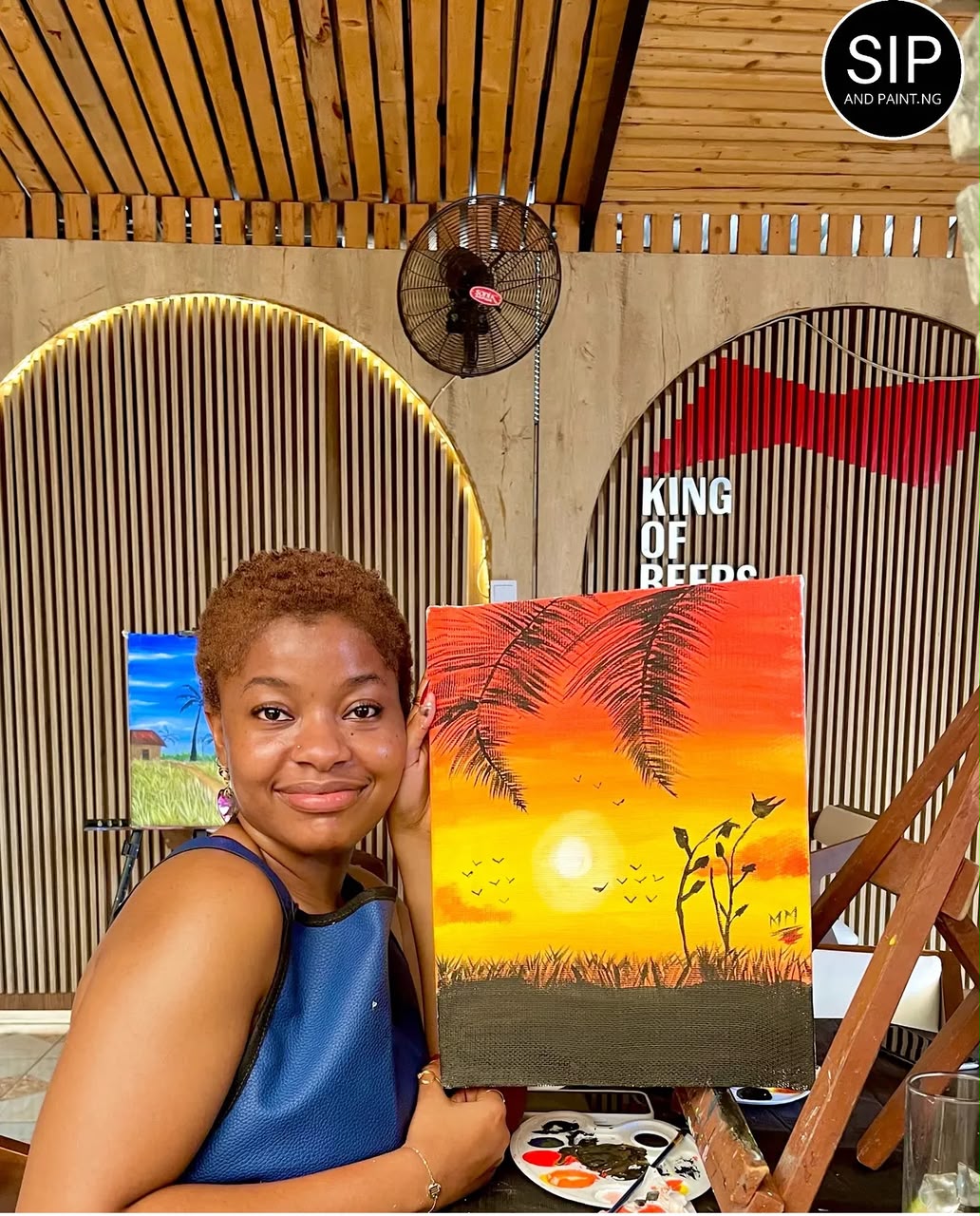 A guest at Pasha Maitama holding her orange and yellow sunset painting