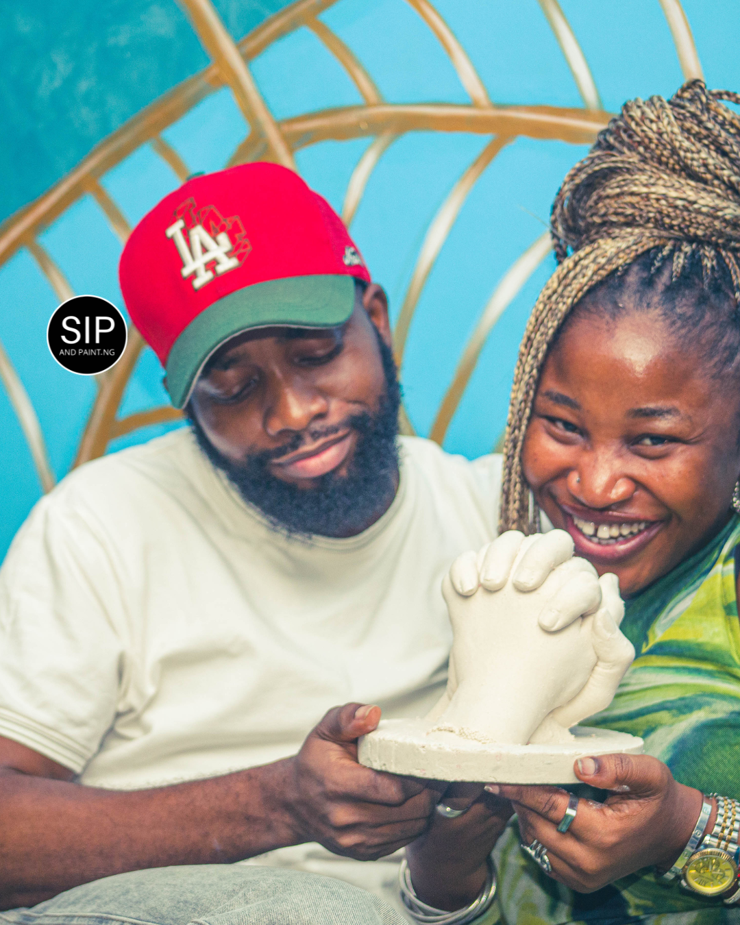 A couple seated together holding a finished white plaster hand cast, both smiling